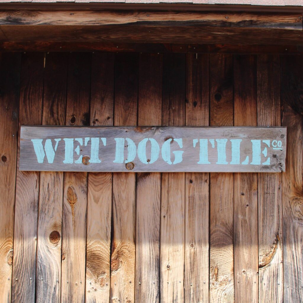 Physical Wet Dog Tile Co logo painted on a wooden sign