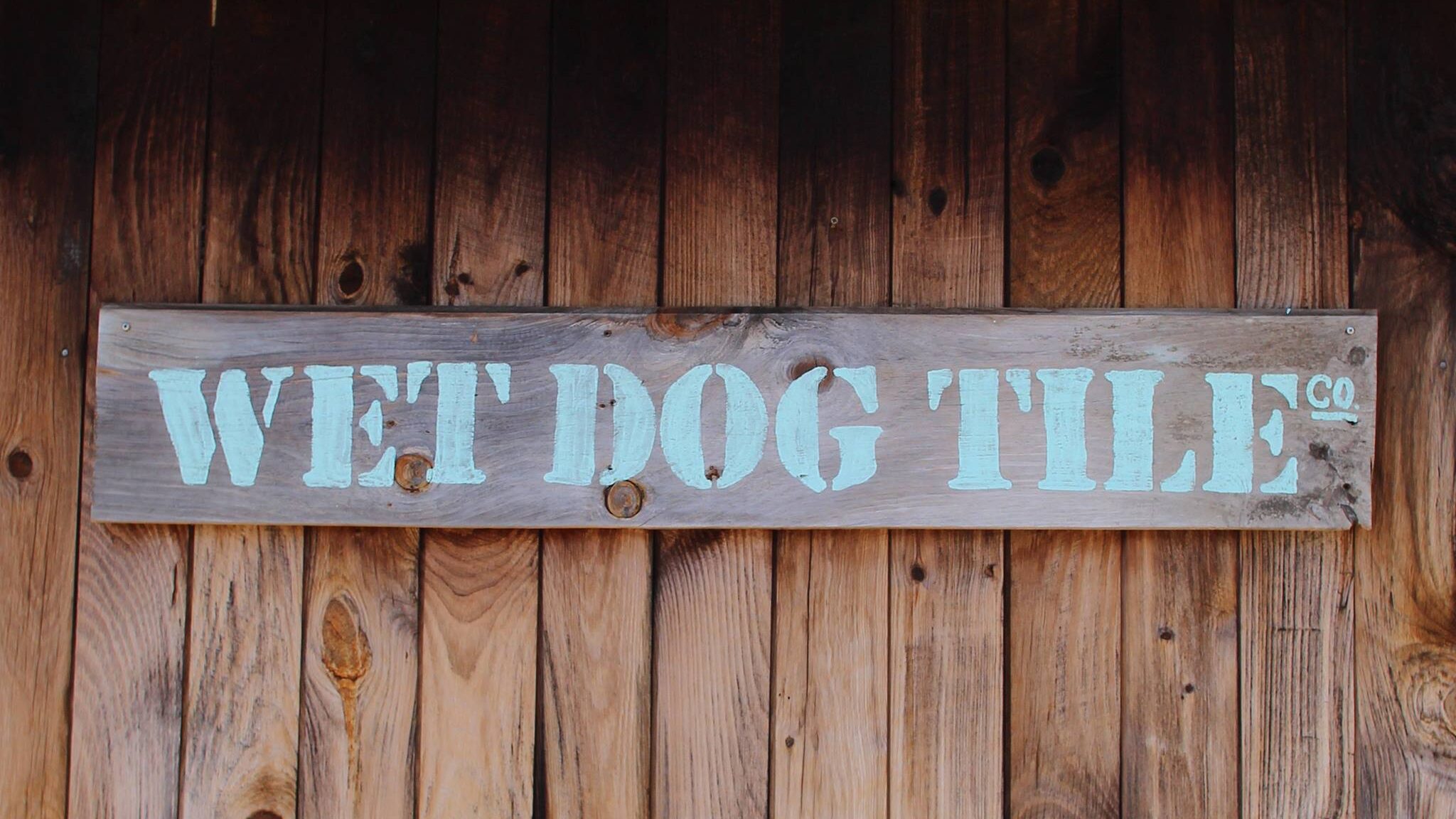 Physical Wet Dog Tile Co logo painted on a wooden sign